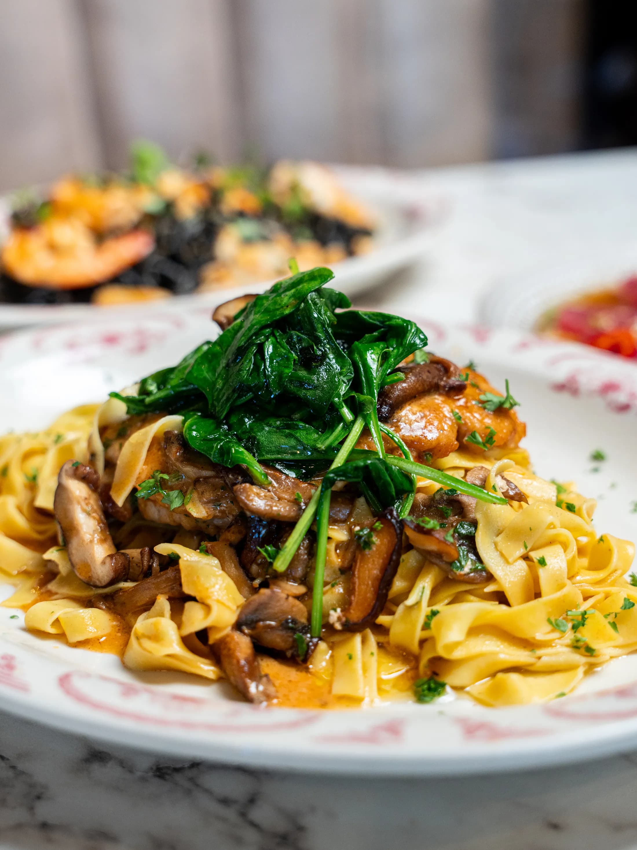 Ribbon pasta with mushrooms and sautéed greens on a rose-patterned plate